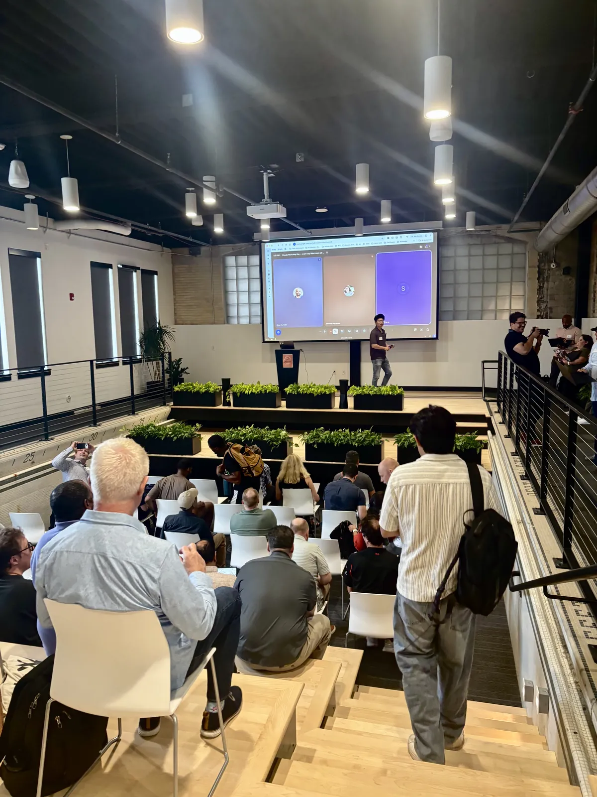 An audience in tiered seating watching a speaker present at a startup event.