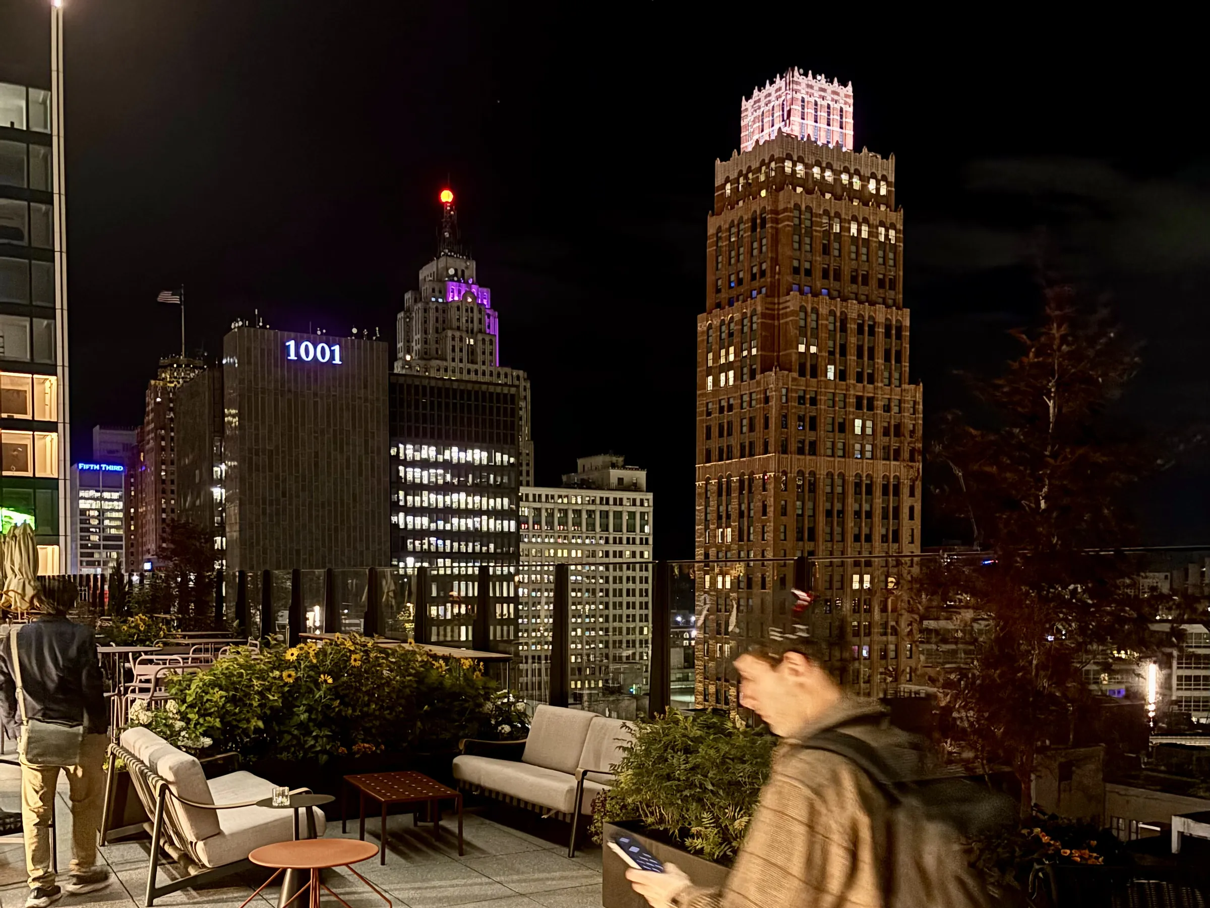 A rooftop lounge in downtown Detroit at night, with the city skyline lit up behind it.