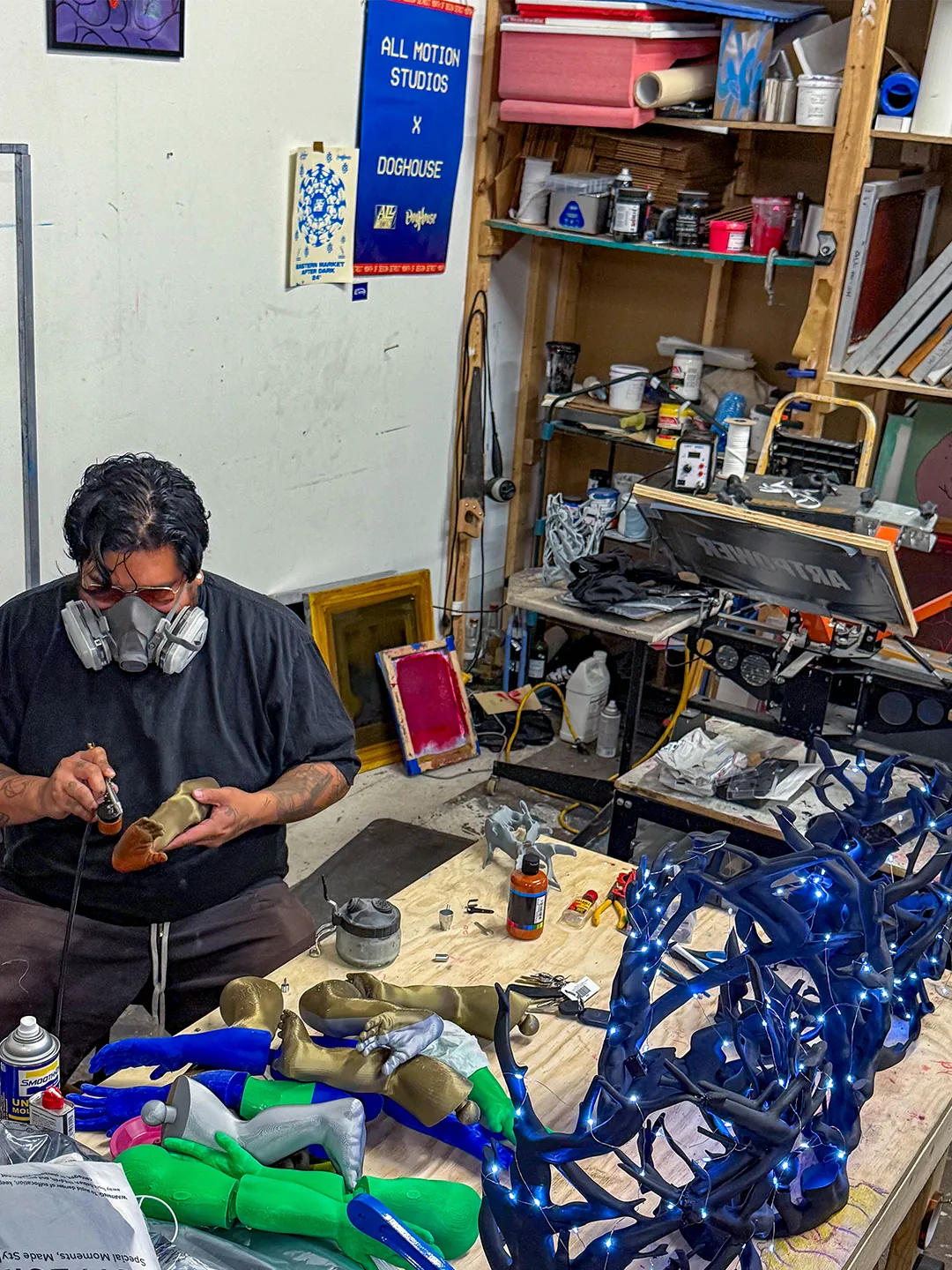 An All-Motion Studio artist in a respirator painting sculpture parts beside the glowing branch headpieces.