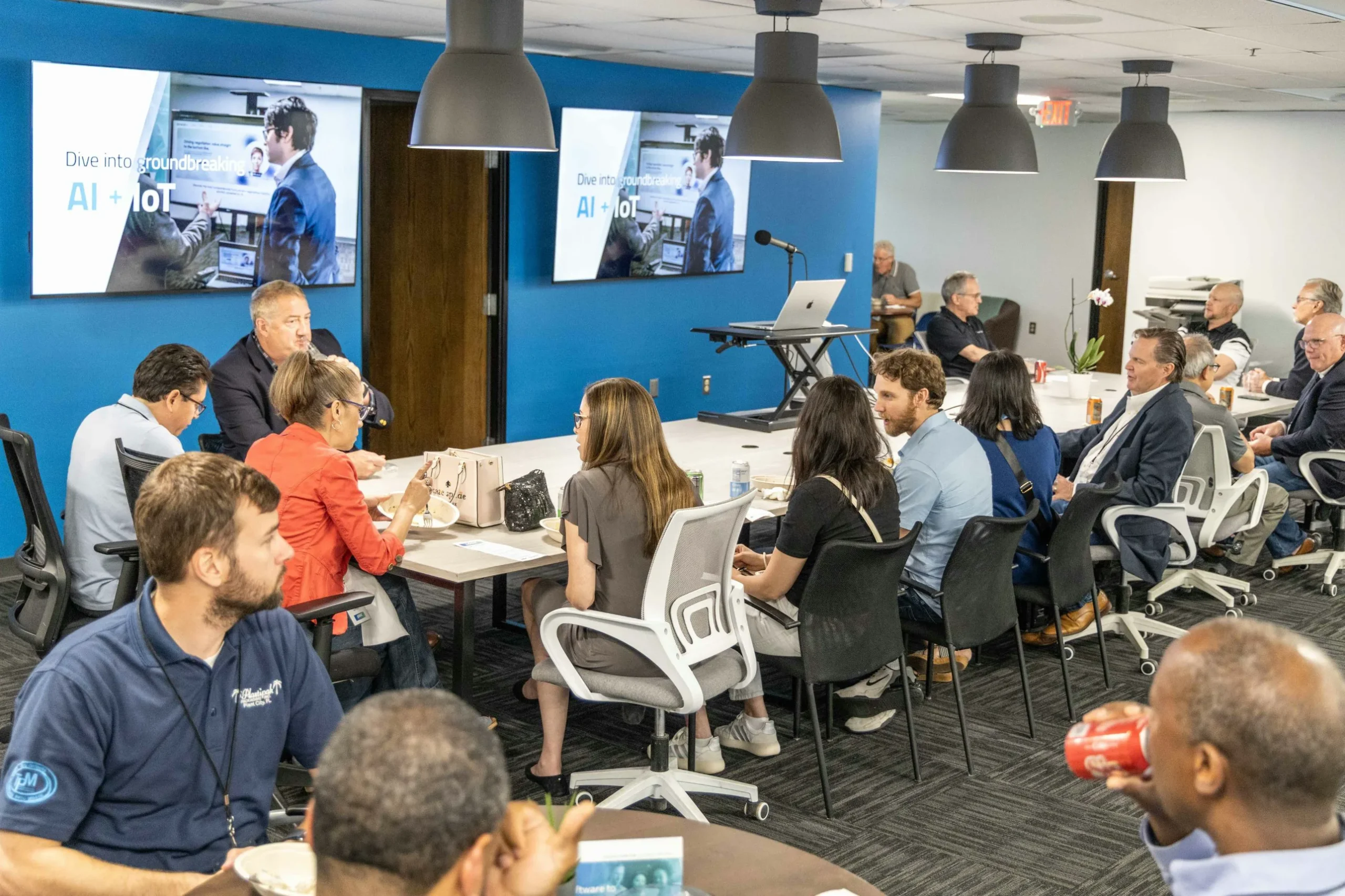 Guests at a Logic Solutions Tech Event talking over dinner, with AI + IoT slides on screens